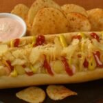 Colombian hot dogs recipe with sausage in a bun topped with pineapple sauce, crushed chips, cheese, and pink sauce