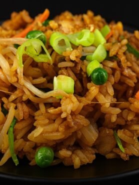 A bowl of fried rice with eggs, peas, carrots, and scallions tossed in soy sauce.