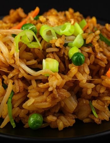 A bowl of fried rice with eggs, peas, carrots, and scallions tossed in soy sauce.