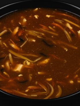 A bowl of hot and sour soup with tofu, mushrooms, and green onions in a rich broth.