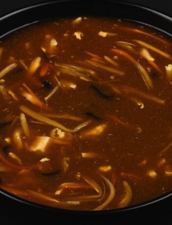 A bowl of hot and sour soup with tofu, mushrooms, and green onions in a rich broth.
