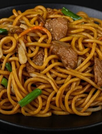 A bowl of lo mein noodles stir-fried with bell peppers, cabbage, carrots, and green onions.