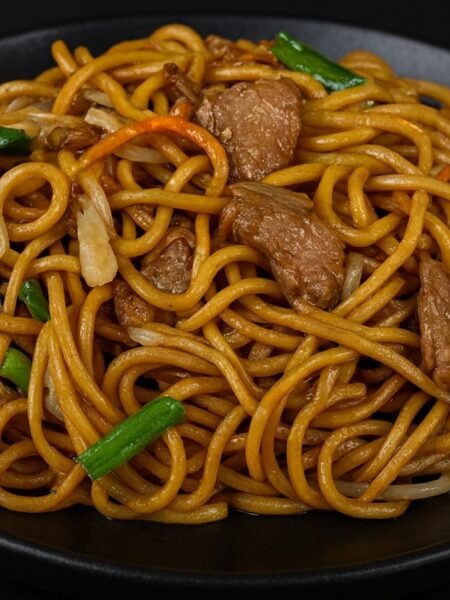 A bowl of lo mein noodles stir-fried with bell peppers, cabbage, carrots, and green onions.