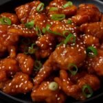 Crispy golden chicken bites coated in a glossy orange sauce and garnished with green onions.