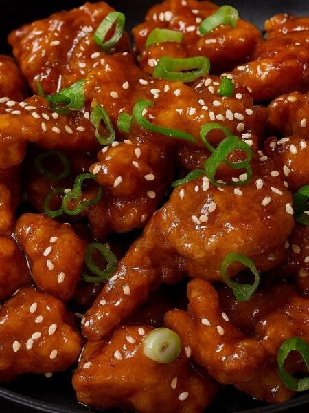 Crispy golden chicken bites coated in a glossy orange sauce and garnished with green onions.