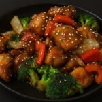 Crispy chicken pieces coated in a glossy sesame sauce and garnished with sesame seeds and green onions.