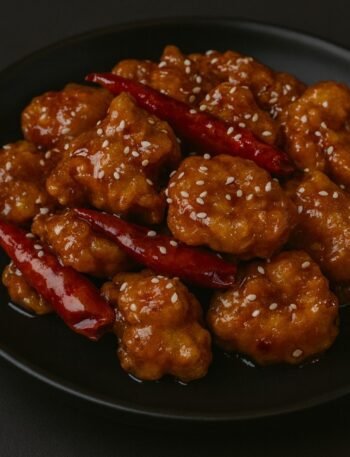 Crispy chicken bites coated in a glossy orange chili glaze, garnished with sesame seeds and green onions.